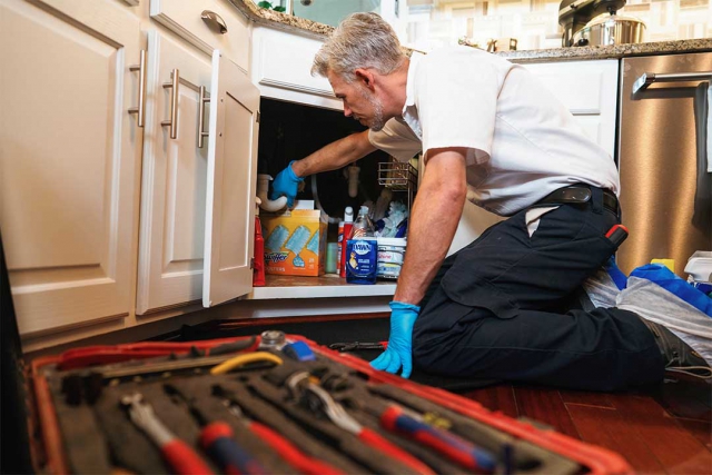 A plumber cleaning the drain of a kitchen sink.